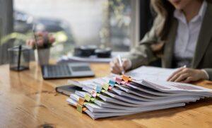 Business Documents concept : Businesswoman working in Stacks of paper files for searching and checking unfinished document achieves on folders papers