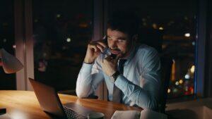 Tired entrepreneur calling partners sitting office desk late evening close up.