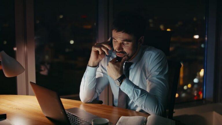 Tired entrepreneur calling partners sitting office desk late evening close up.