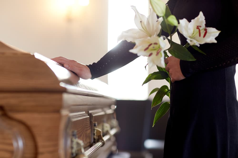 a person holding a flower and standing in front of a coffin