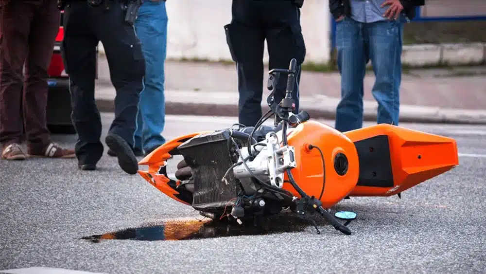 Orange motorcyle lying on its side and leaking oil after being involved in an accident
