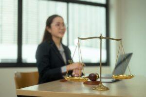 Golden balance scales on wooden table against professional lawyer sitting in background. Law and justice concept