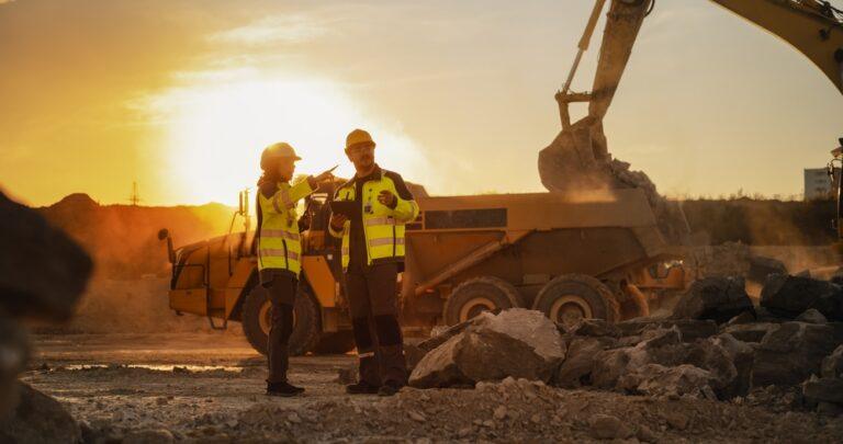 Two construction professionals review plans on an active job site, with one wondering whether a subcontractor can be sued after a construction injury.