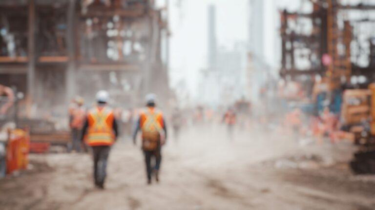 Construction workers in safety vests walk through a job site where the property owner is liable for any unsafe conditions. 