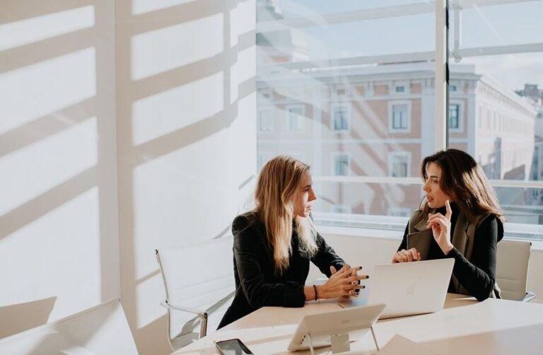 Two female office workers having a conversation. Find out what happens if your employer pressures you not to file a workers’ comp claim.