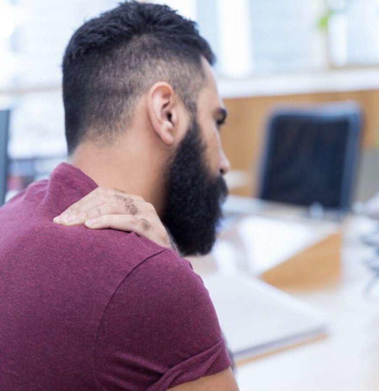 A man rubbing his shoulder and wondering what happens if his job aggravates an old neck or back injury.