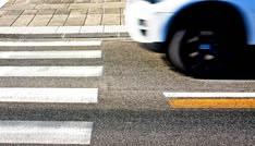 A rideshare car stops at a marked crosswalk as two pedestrians wait to cross the street. Uber and Lyft drivers must yield to pedestrians when required under New York traffic laws.