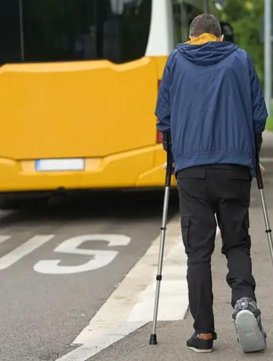Rear view of an injured male walking to a bus stop using crutches because the insurance company sent him to physical therapy too far away from home.